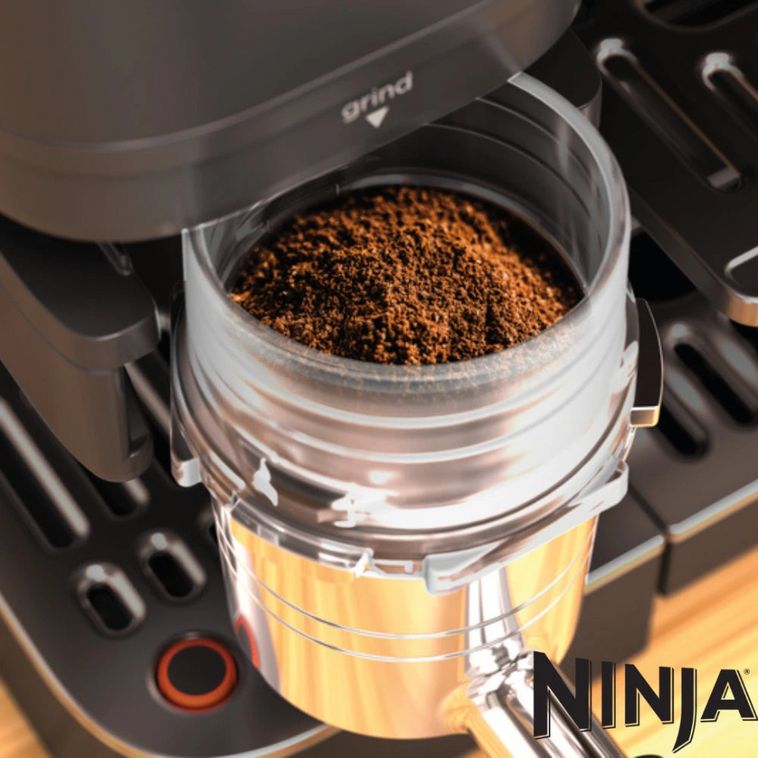 Ninja Luxe Café Premier Series coffee machine with freshly ground coffee in transparent brew basket, black and gold design with orange accent button visible