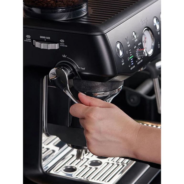 Hand operating the group head lever on a black Sage Barista Express Impress espresso machine with illuminated drip tray, showing control panel with dials and buttons above