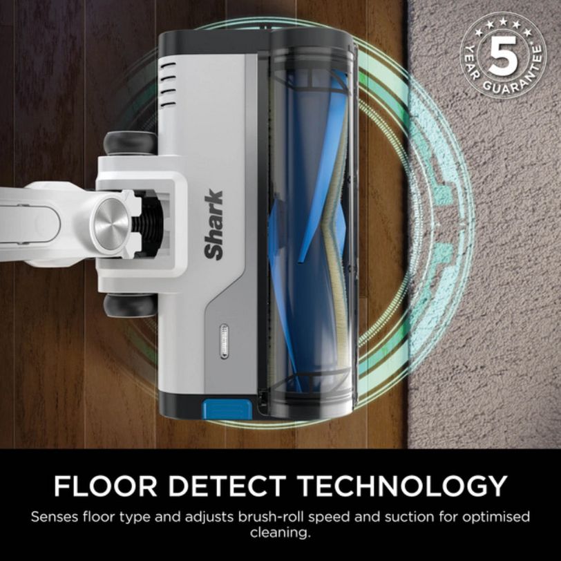 Shark PowerPro cordless stick vacuum cleaner in white and black with transparent dust bin, shown from above on wooden and carpeted flooring, featuring Floor Detect Technology diagram with 5 year guarantee badge