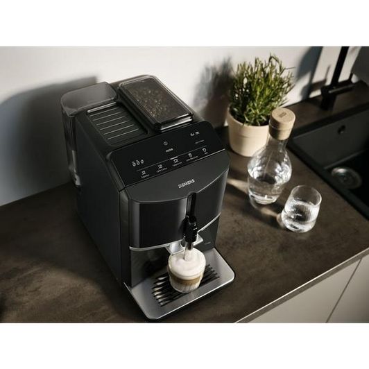Siemens EQ300 black fully automatic bean to cup coffee machine dispensing cappuccino on kitchen counter with water glasses and potted plants