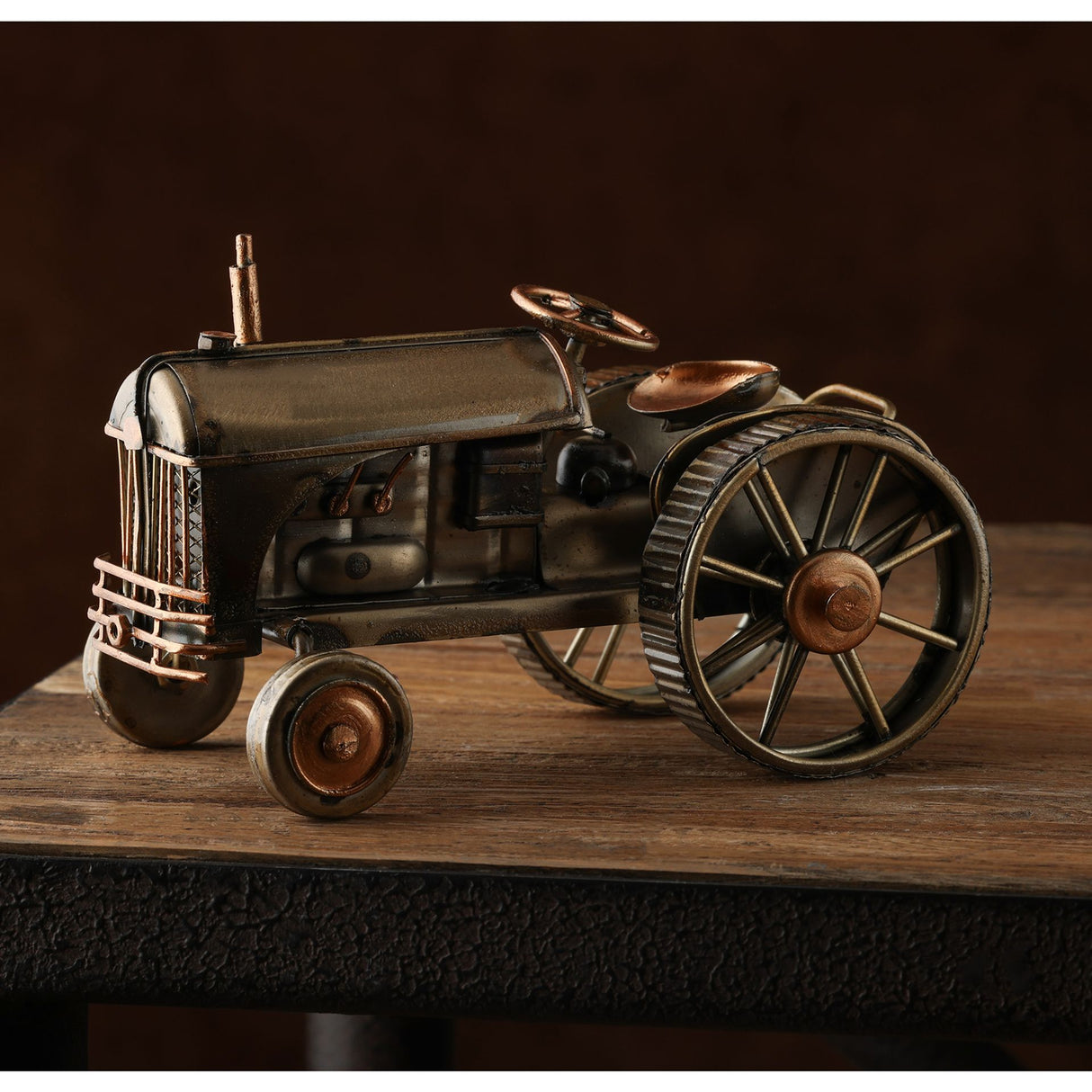 Vintage-style metal tractor ornament with bronze and brass patina finish, featuring detailed wheels, steering wheel, and exhaust pipe, displayed on wooden surface against dark background