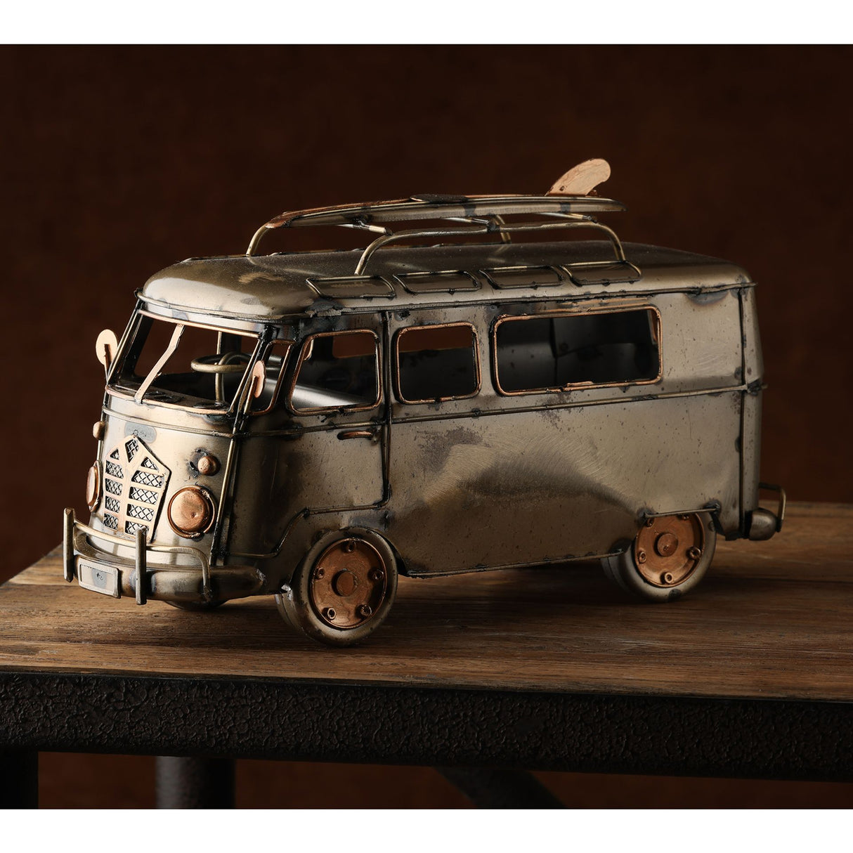 Vintage metal campervan ornament with silver and bronze finish, featuring detailed windows, roof rack with surfboard, and weathered patina, displayed on wooden surface against dark background