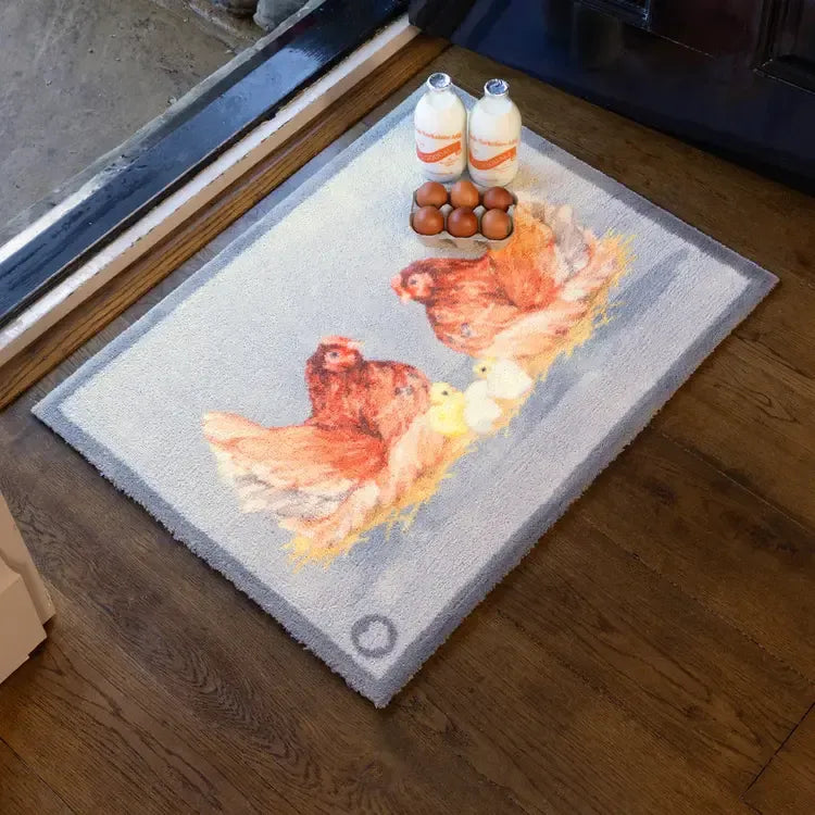 Hug Rug doormat 65cm x 85cm featuring Mother Hens design with two brown chickens in red and yellow tones on grey background, displayed with milk bottles and brown eggs, hardwearing natural fibre mat on wooden floor