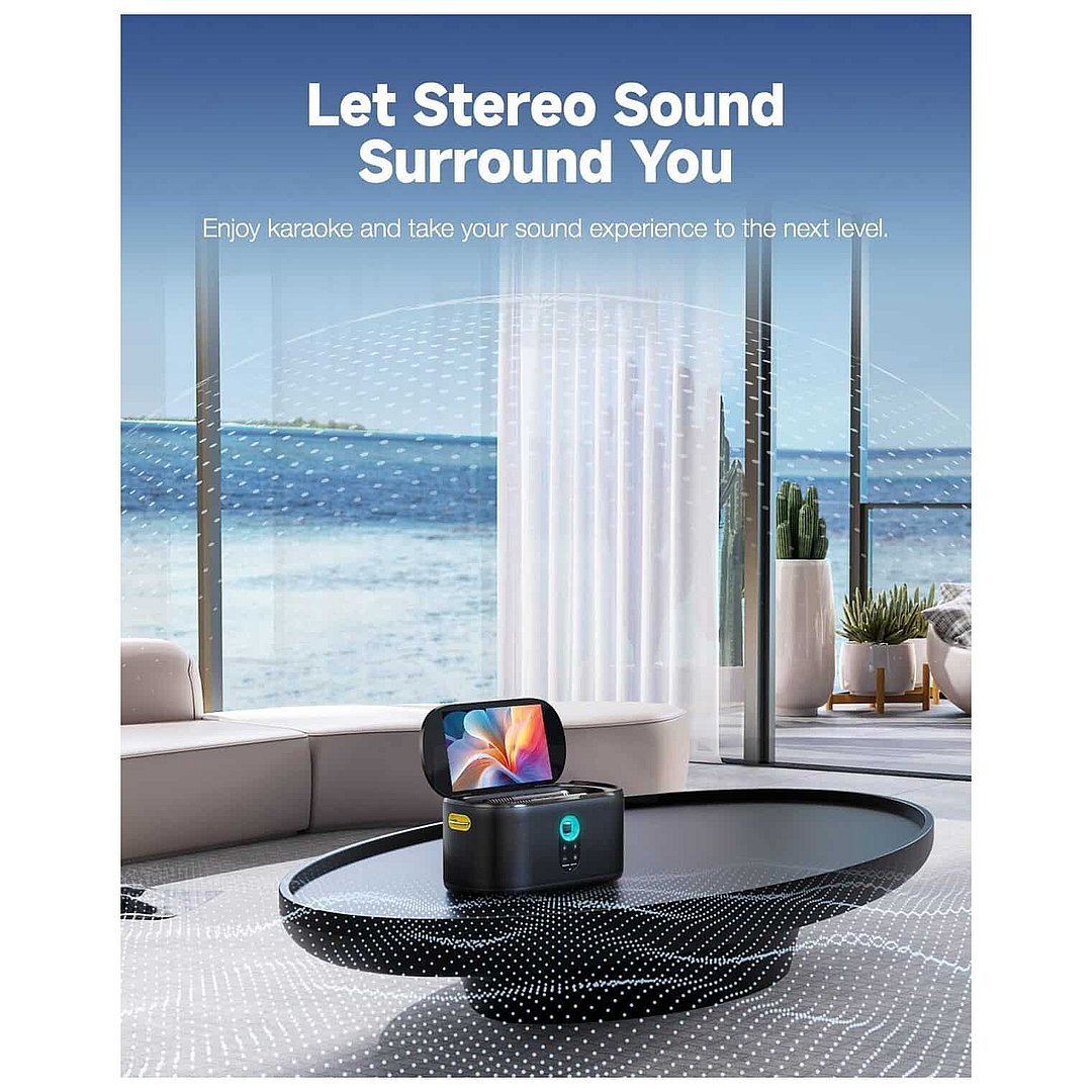 Ikarao Shell S1 Premium portable karaoke machine with black perforated metal base and 10.1 inch HD screen displaying colorful interface, positioned on modern living room floor with ocean view through floor-to-ceiling windows, beige sofa and potted plants in background, promoting stereo sound and karaoke experience