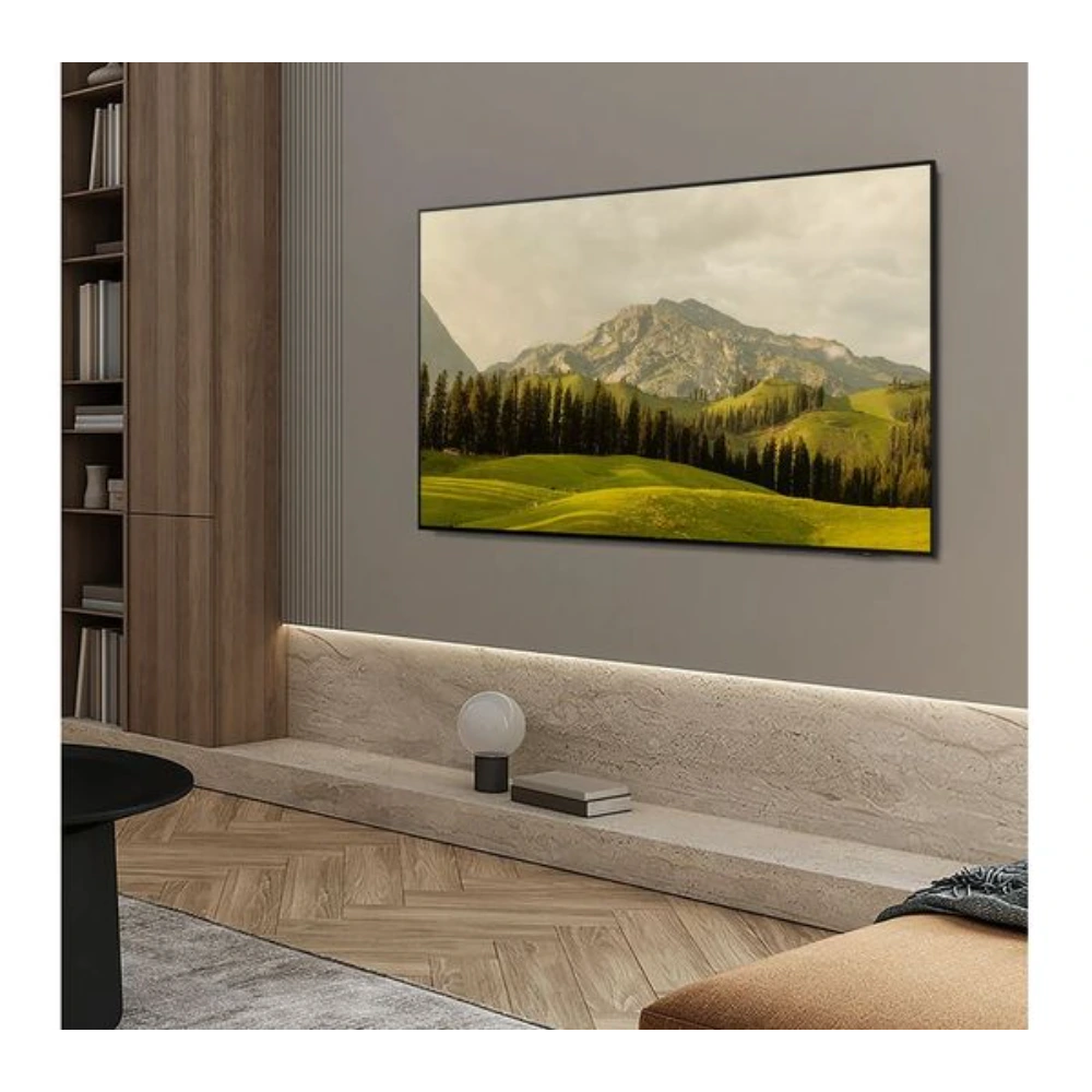 Samsung S85F 77 inch 4K OLED Smart TV mounted on grey wall above wooden console table in modern living room with wooden shelving, displaying landscape image of green mountains and forest
