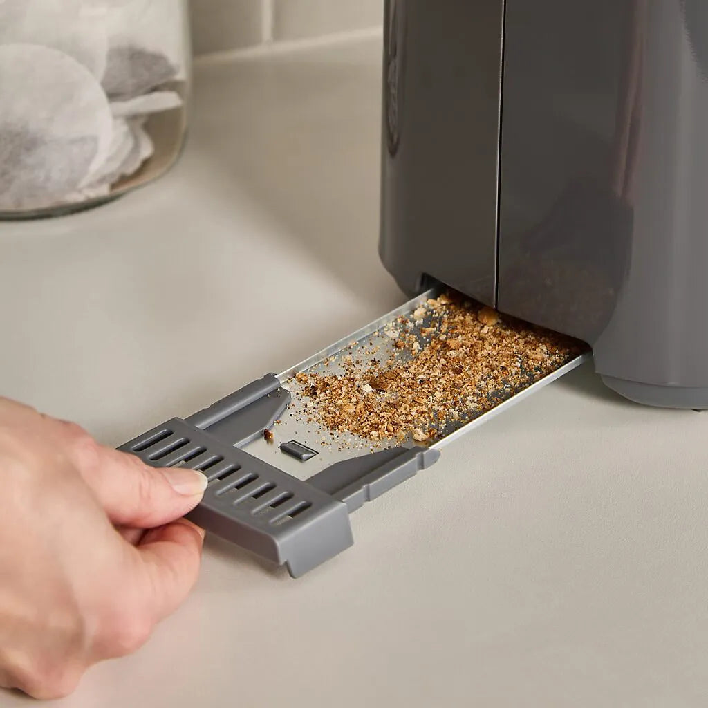 Hand pulling out crumb tray from grey Morphy Richards Equip 2 slice toaster showing collected breadcrumbs and debris on white kitchen counter