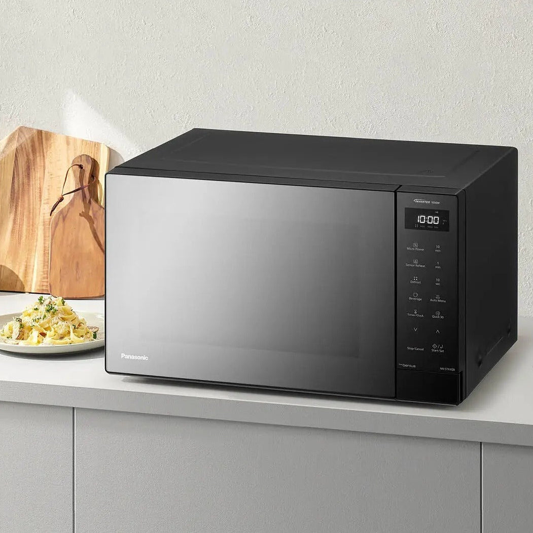 Panasonic 32 litre black invertor solo microwave with mirror door and digital display on kitchen counter next to wooden chopping board and plate of food