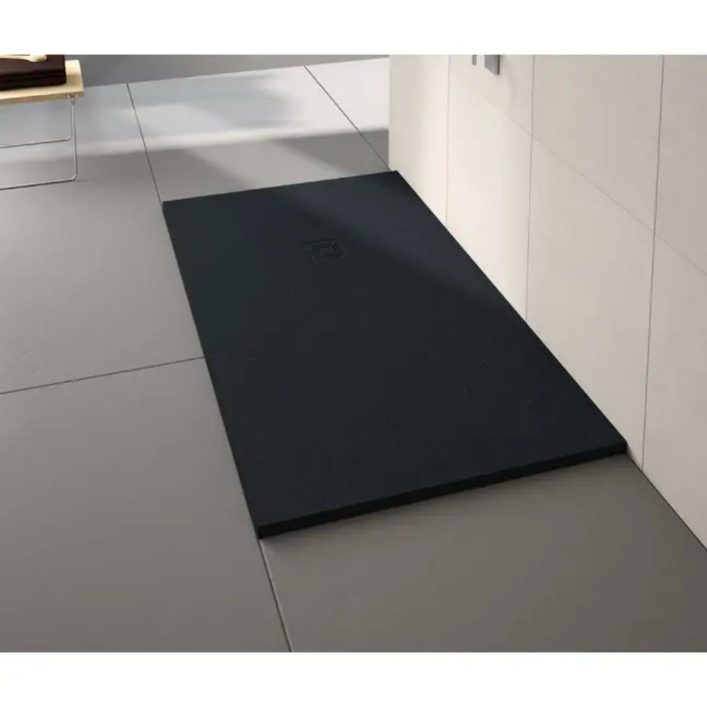 Black rectangular stone shower tray with drain inset, positioned in modern white tiled bathroom with white wall paneling