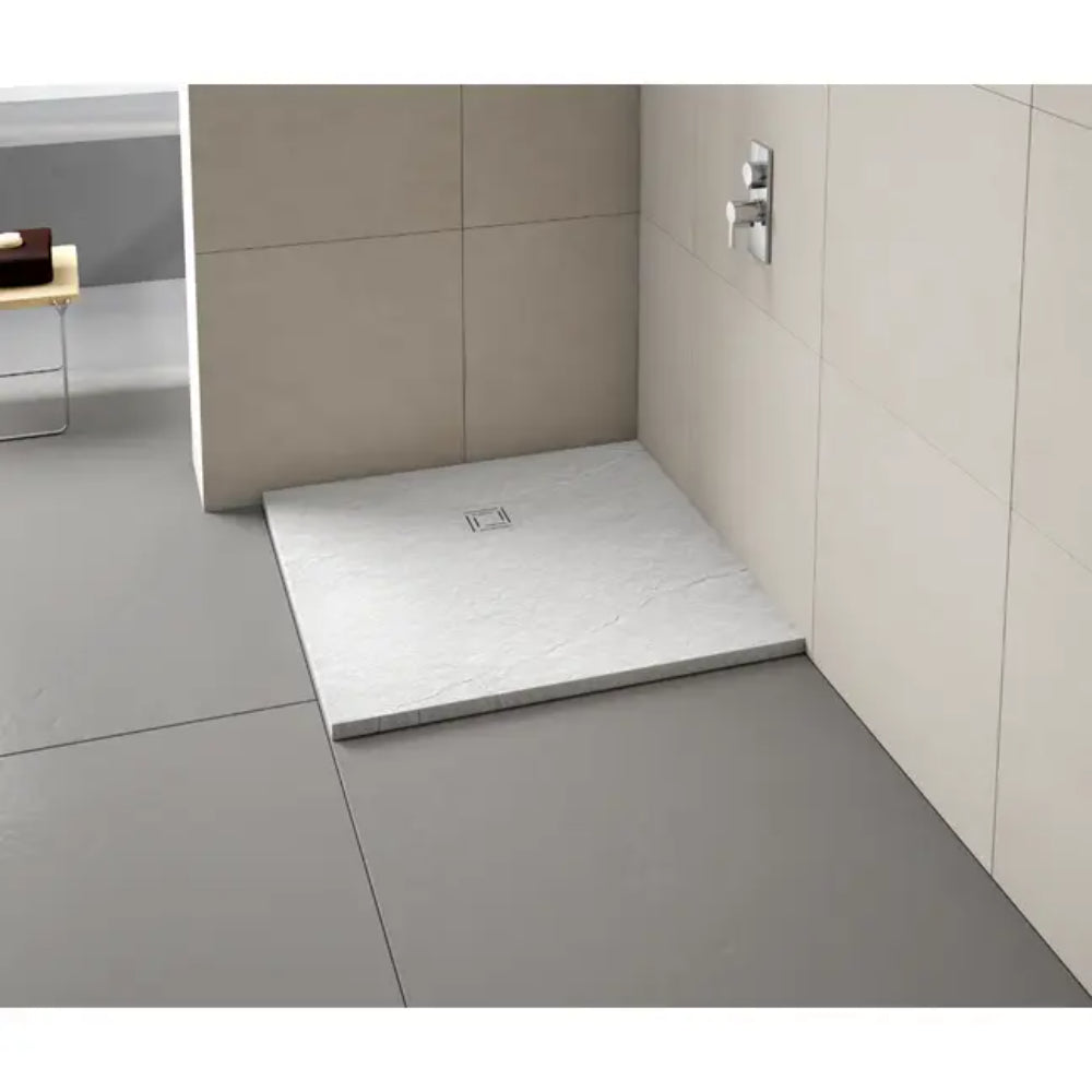 Modern bathroom shower enclosure featuring a white rectangular Merlyn Truestone shower tray with integrated drain, set within beige and cream tiled walls and grey floor tiles, chrome shower valve visible on right wall