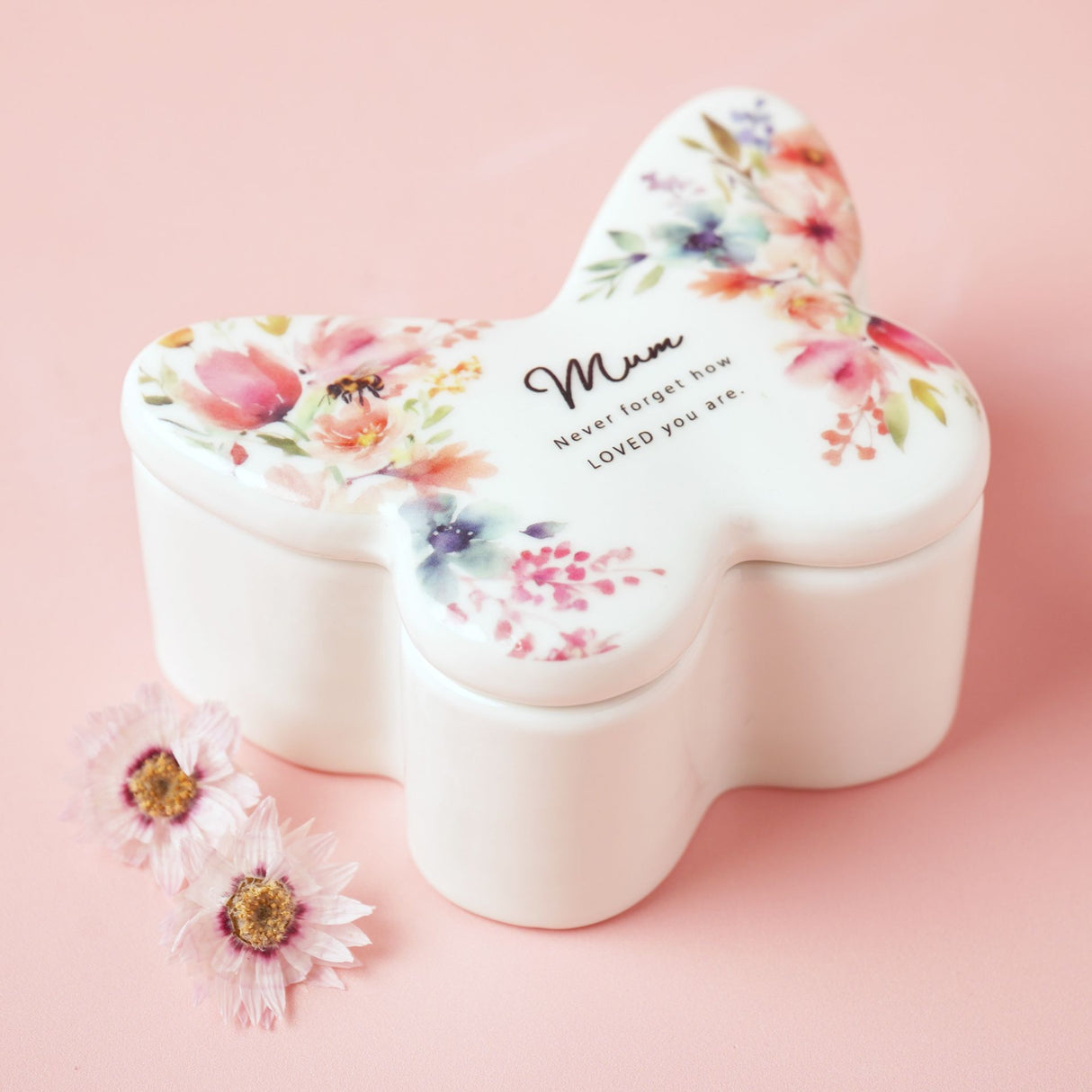 Floral-patterned butterfly-shaped container with 'Mum, never forgot how loved you are' text on a pink background.