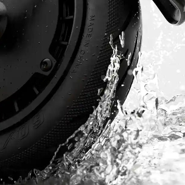 Close-up of black Segway Ninebot electric scooter tire splashing through water, showing textured tread pattern and water droplets in black and white photography