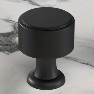 Black cylindrical kitchen cabinet door knob with pedestal base on marble surface