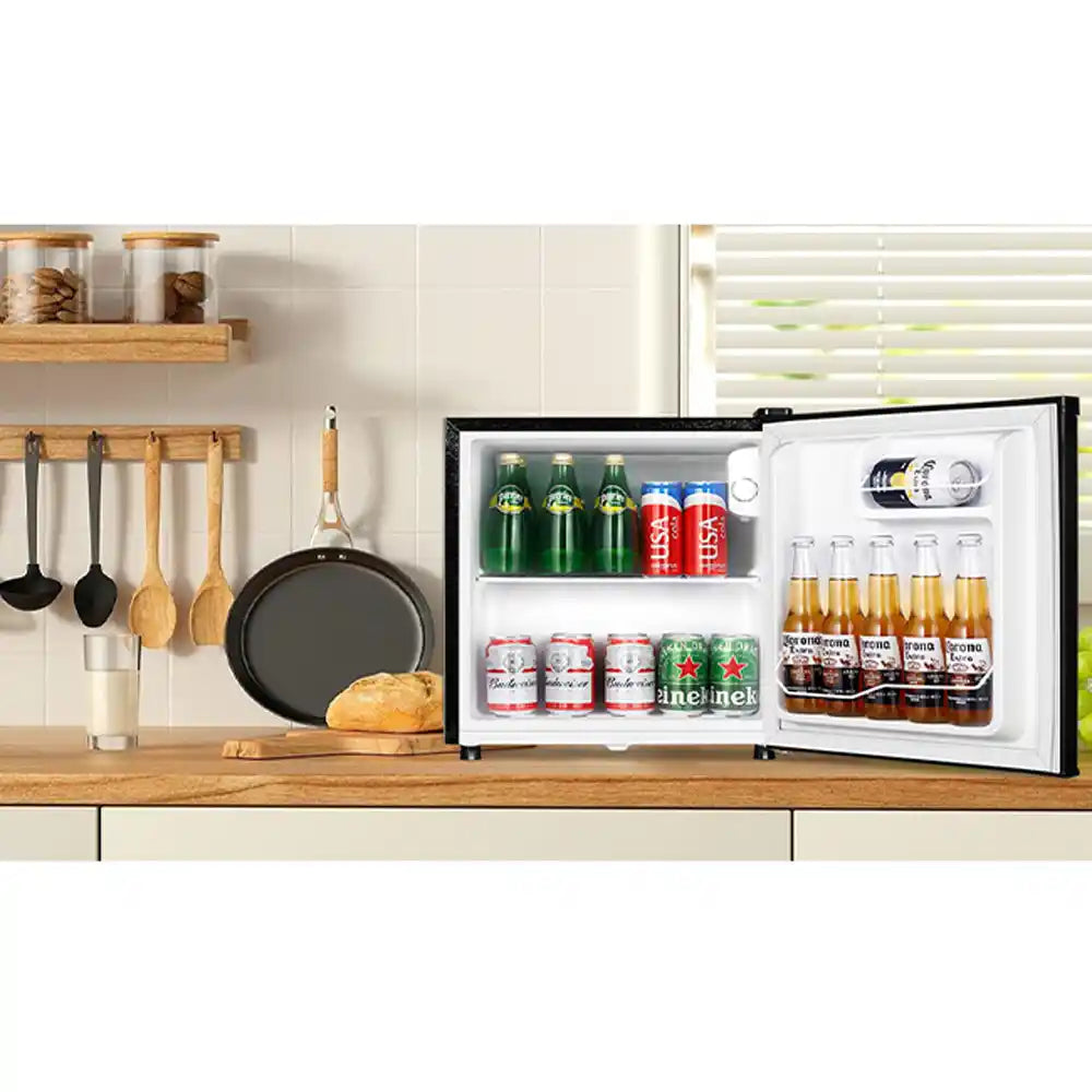 Black tabletop mini fridge with 51 litre capacity displayed on wooden kitchen counter next to cooking utensils, containing beverages and canned drinks with open door showing white interior shelving