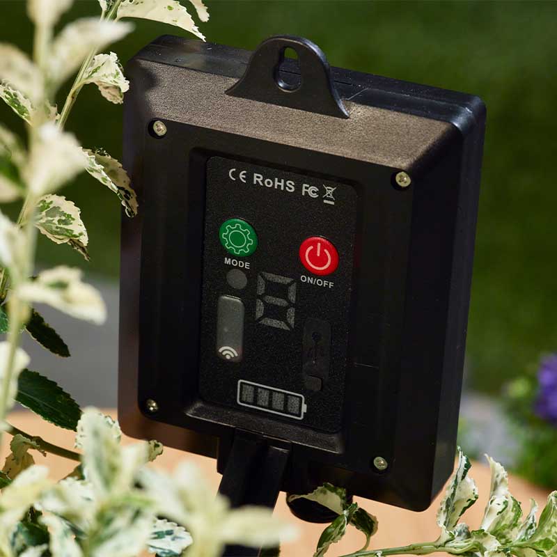 Close-up of black wireless control unit mounted on garden plant with green MODE button and red ON/OFF power button, showing CE RoHS FCC certification marks for Smart Garden festoon string lights