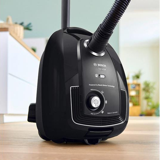 Black Bosch garment steamer on a wooden surface with a blurred indoor background