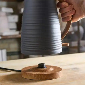 Morphy Richards Clay Flint grey jug kettle being poured onto wooden base, showing stainless steel spout and wood grain detail on 1.7 litre capacity kettle