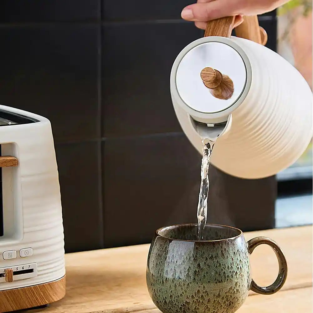 Morphy Richards Clay Flint white jug kettle pouring hot water into a textured grey ceramic mug on a wooden surface next to a matching white kettle with wooden accents