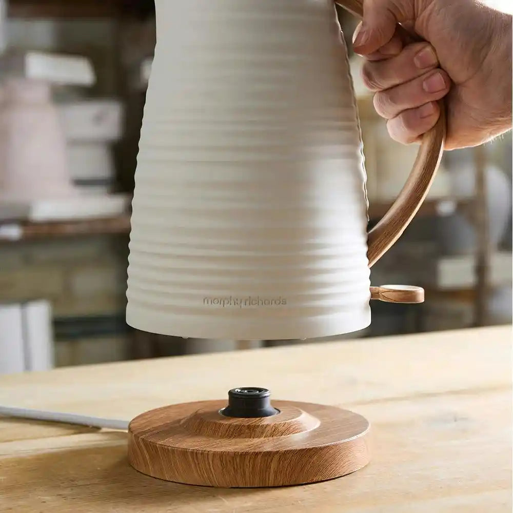 Morphy Richards Clay Flint white jug kettle with wooden handle and base being held over wooden surface in kitchen setting