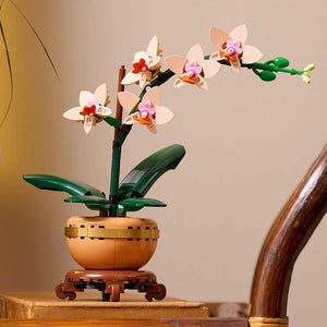 LEGO Mini Orchid 10343 set displaying constructed white and pink orchid flowers with orange centers in a tan and brown decorative pot with green leaves on a wooden surface