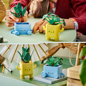 LEGO Happy Plants set 10349 featuring two buildable potted plant characters with smiling faces - one blue pot with wheels on wheels holding green leafy stems, one yellow pot with arms holding green foliage, displayed on a table during playtime with children in colorful clothing