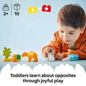 Young toddler in orange shirt playing with colorful LEGO Wild Animal Families set featuring orange lion and penguin figures, green plant, and blue building blocks on white surface against light blue background, with age 2+ and 10 piece count indicators