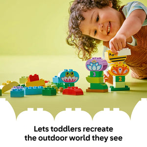 Toddler with curly hair playing with colorful LEGO Creative Garden and Flowers building set featuring lotus flowers and numbered stacking pieces in bright green, blue, purple, red and yellow on yellow background