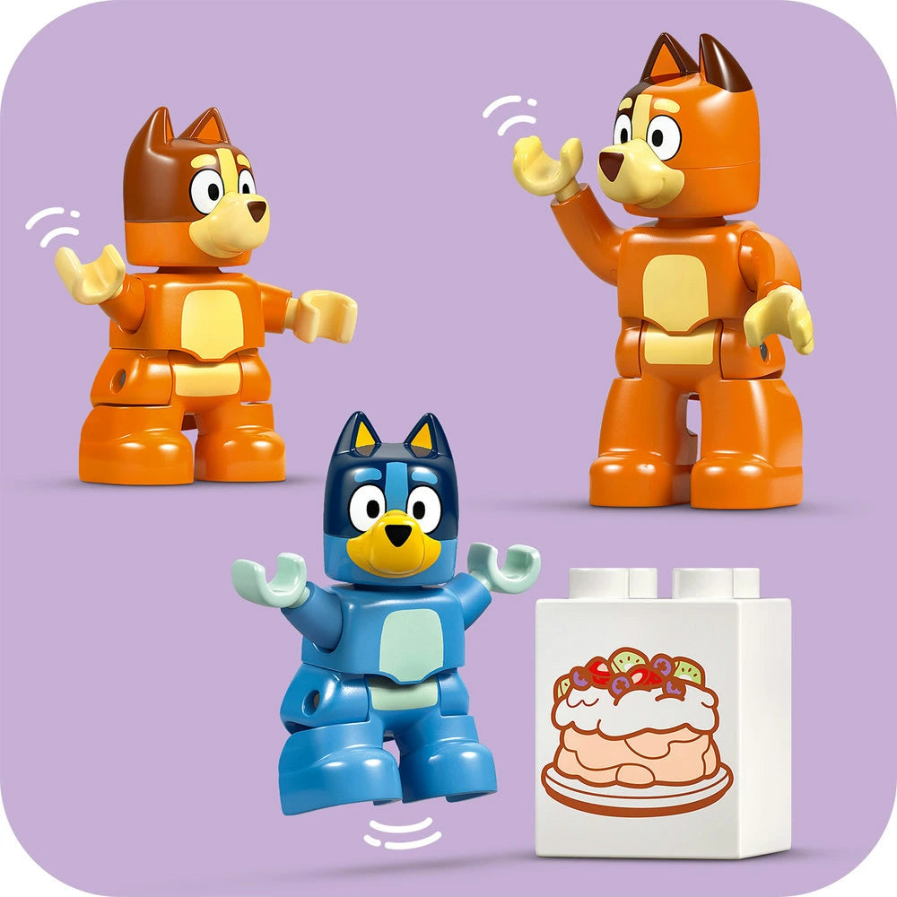 LEGO Bluey Family House building set featuring three colorful LEGO minifigures - two orange and yellow dog characters and one blue dog character with articulated arms - alongside a white LEGO brick element decorated with an illustrated cake design, displayed against a purple background