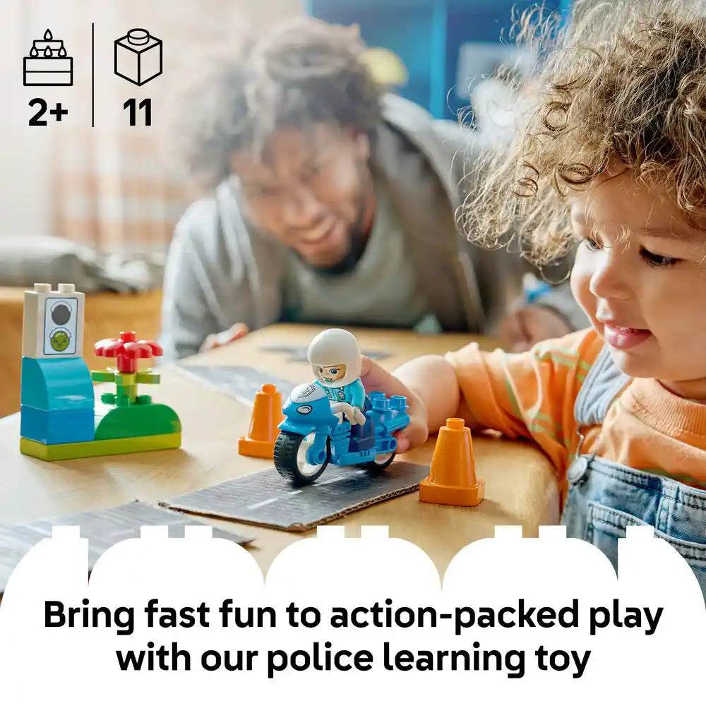 Young child in orange shirt playing with blue LEGO police motorcycle set at wooden table with elderly caregiver, featuring traffic cones and flower elements, age 2+ with 11 pieces