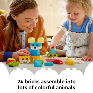Adult and toddler playing with colorful LEGO DUPLO brick animals including a blue mouse with yellow ears, yellow cat face, and green caterpillar made from 24 large building blocks on white surface