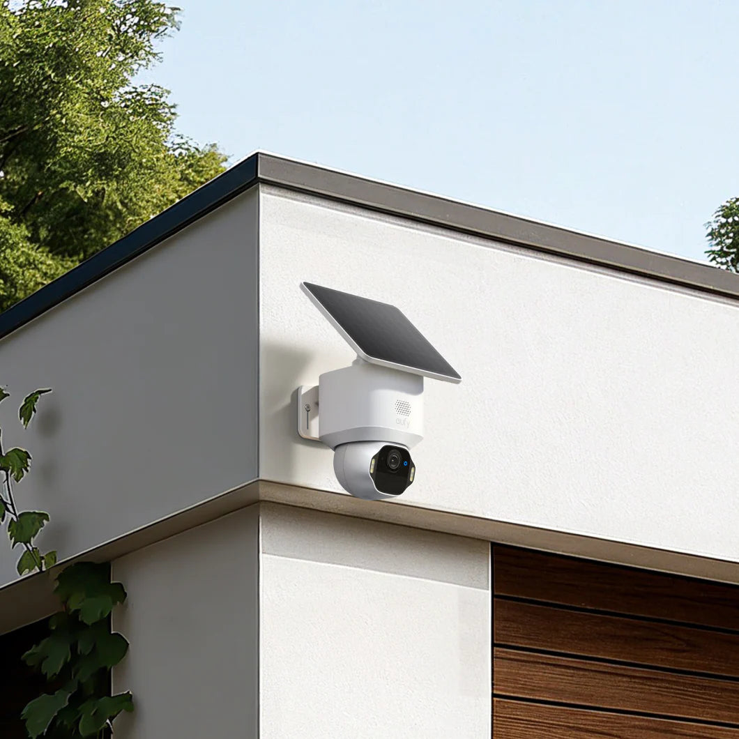 Solar-powered security camera on a house exterior with greenery in the background