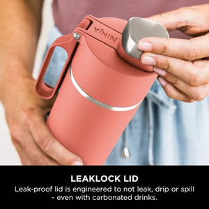 Person holding coral-colored Ninja Thirsti 530ml insulated travel bottle with leaklock lid open, displaying gray interior cup and leak-proof design feature against blurred background