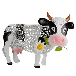 Decorative solar garden cow silhouette with black and white coloring, ornate gray metal filigree body panel, pink nose and udder, brown horns, holding a white daisy flower with yellow center