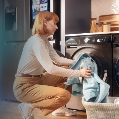 Woman loading laundry into a washing machine in a kitchen.