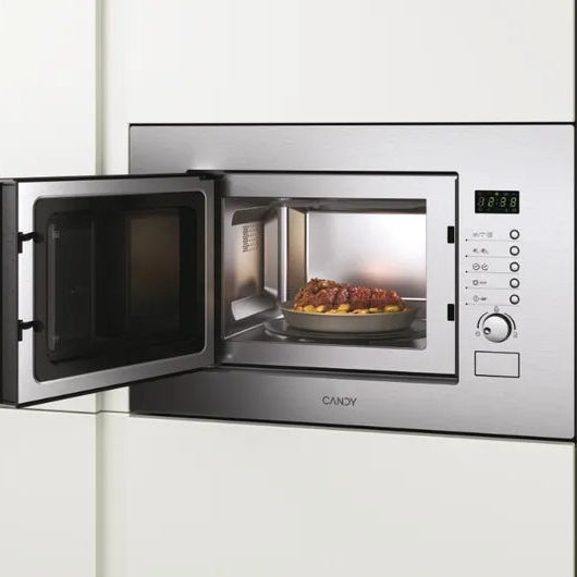 Candy 20 litre built-in microwave with grill in stainless steel featuring open door with food inside, digital display, control panel with buttons and dial, mounted in white kitchen cabinetry