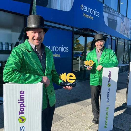 Two men in green jackets holding awards in front of a Euronics store.