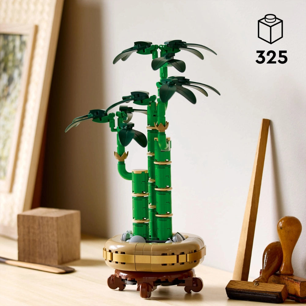 LEGO Lucky Bamboo set 10344 displayed on wooden desktop featuring green segmented bamboo stalks with dark green leaves, tan and brown circular pot base, surrounded by wooden desk accessories including blocks and brushes, 325 pieces