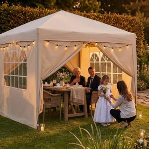 Cream Euroactive pop up gazebo with sidewalls set up on garden lawn at dusk, featuring string lights and sheer curtains, with family gathered inside around wooden table for outdoor celebration