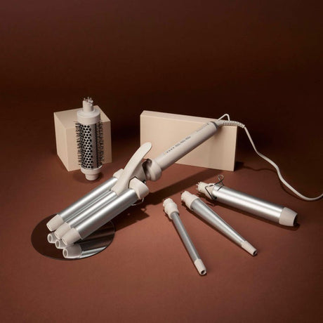 Remington Trendology 5-in-1 hair curler set in silver and cream with interchangeable barrel attachments, cylindrical brush, power cord and storage case on brown background