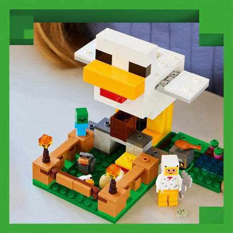 LEGO Minecraft Chicken Farm set 21585 featuring a white and yellow barn structure with a chicken coop, green baseplate with fencing, minifigures including a farmer character, orange and brown terrain pieces, and flame torches displayed against a blurred background