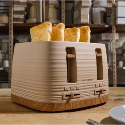 Morphy Richards Clay Felspar 4 slice toaster with cream and wood finish, displaying four golden toasted slices of bread in the slots, shown on a kitchen countertop with blurred appliances in the background
