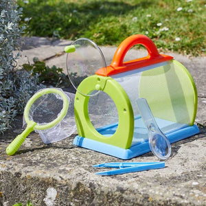 Colorful bug catching kit for children featuring a bright lime green and blue mesh habitat box with red carrying handle, accompanied by a matching green net, magnifying glass, tweezers and specimen tube, displayed on garden paving with plants in background