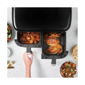 Russell Hobbs Satisfry Dual Basket Air Fryer displaying two black removable baskets with cooked chicken breasts in right basket and roasted potatoes in left basket, shown from overhead on white speckled countertop with fresh salads and bread surrounding the appliance