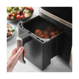Russell Hobbs Satisfry black dual basket air fryer with 9 litre capacity, showing open drawer containing cooked food, displayed on kitchen counter with colorful salad bowls in background