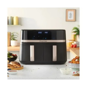 Russell Hobbs Satisfry Dual Basket Air Fryer 9 litre in black with stainless steel accents displayed on a kitchen counter surrounded by cooked food, plants and kitchen accessories