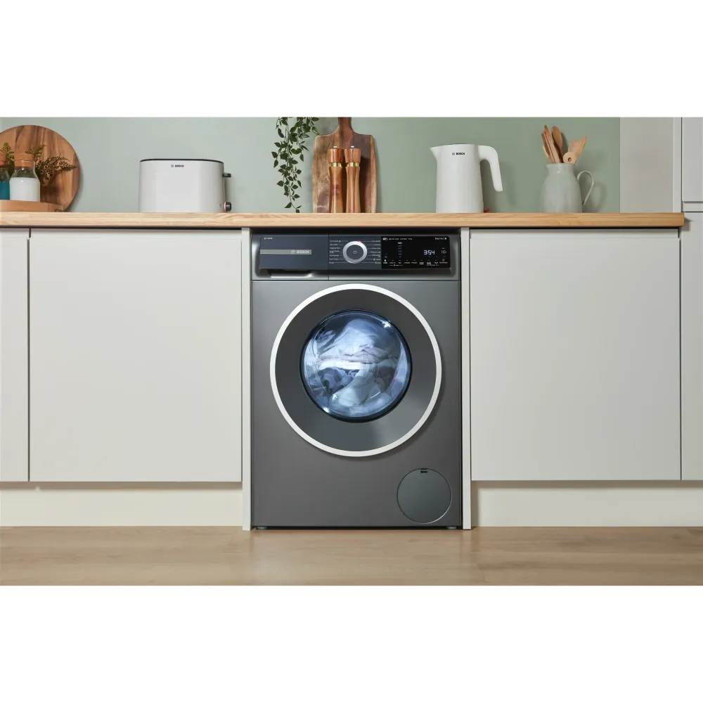 Bosch Series 6 grey washing machine with 10kg capacity and 1400 spin integrated into white kitchen cabinetry with wooden shelf and accessories above
