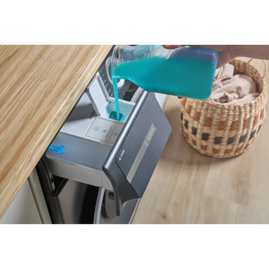 Bosch Series 6 grey front-load washing machine with turquoise detergent dispenser drawer open, displayed on wooden floor next to woven storage basket containing white laundry