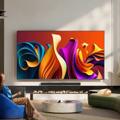 Modern living room with a large flat-screen TV displaying colorful abstract art, a person sitting on a blue chair in the foreground.