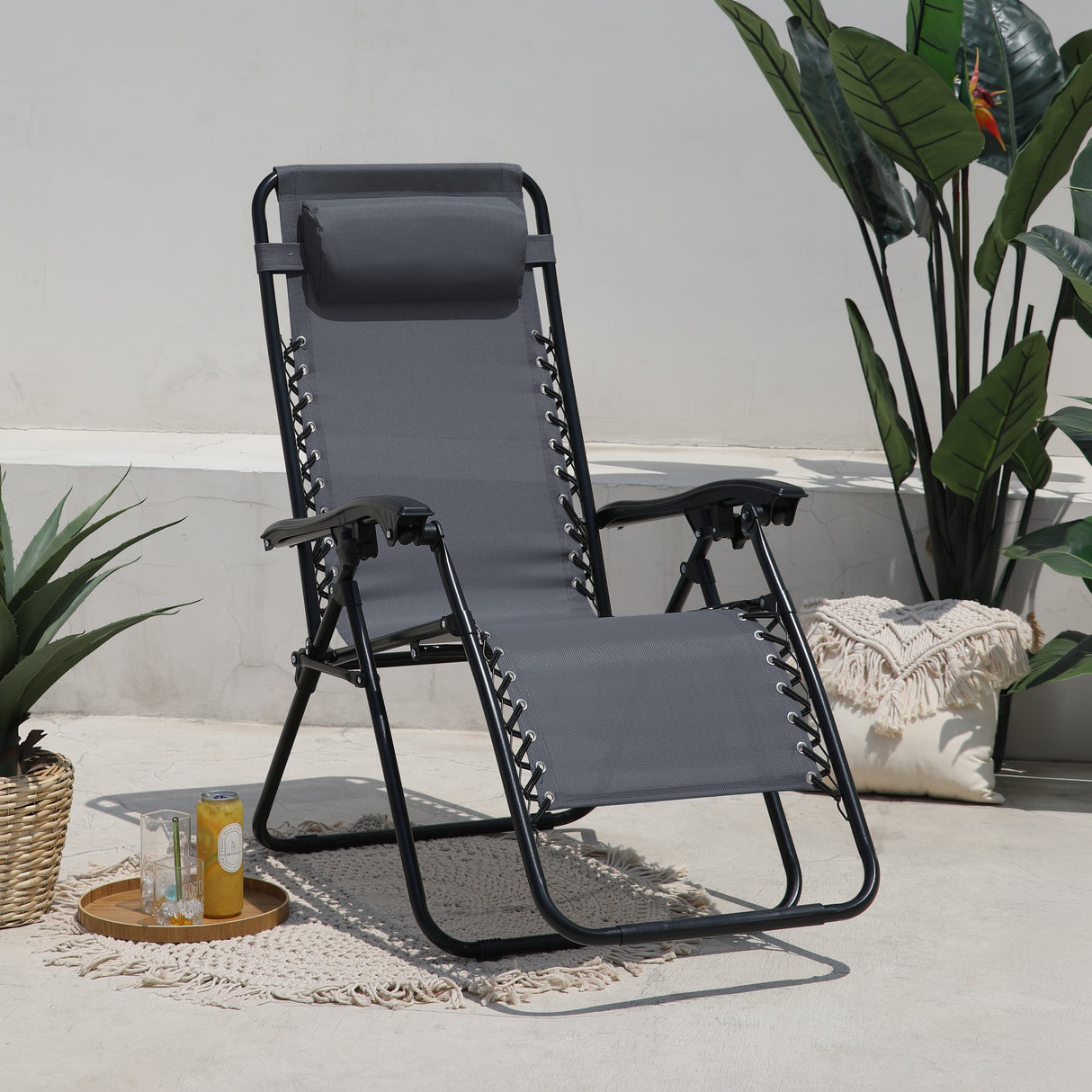 Euroactive Zero Anti Gravity Recliner Chair in graphite grey with black metal frame, featuring adjustable lace-up straps and padded headrest, displayed on a patio setting with potted plants, cushions and refreshments