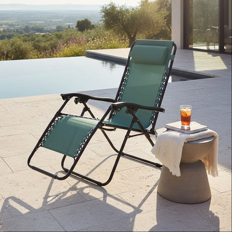 Green and black zero gravity recliner chair on a poolside terrace with infinity pool, countryside views, ceramic side table with beverage and towel, modern outdoor furniture setup