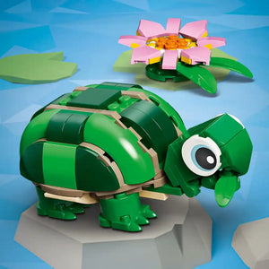 LEGO Creator set 31377 featuring a green brick-built turtle with tan accents and large blue eyes on a gray platform, accompanied by a pink and yellow flower with green leaves against a blue background